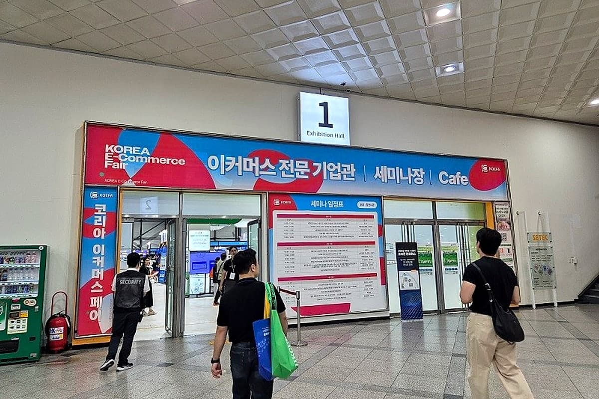 코리아 이커머스 페어 1전시관 입구 — '이커머스 전문 기업관 · 세미나장' 현수막과 세션 일정표 앞을 지나는 참관객들